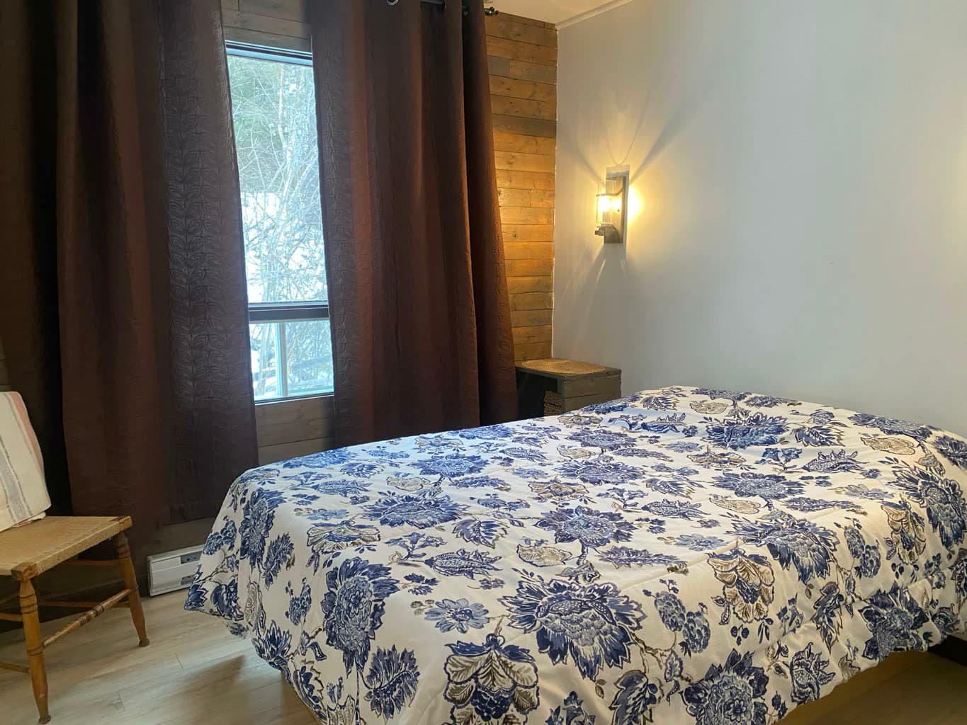 Chambre avec lit double et couvre-lit fleuri bleu, mur de bois.