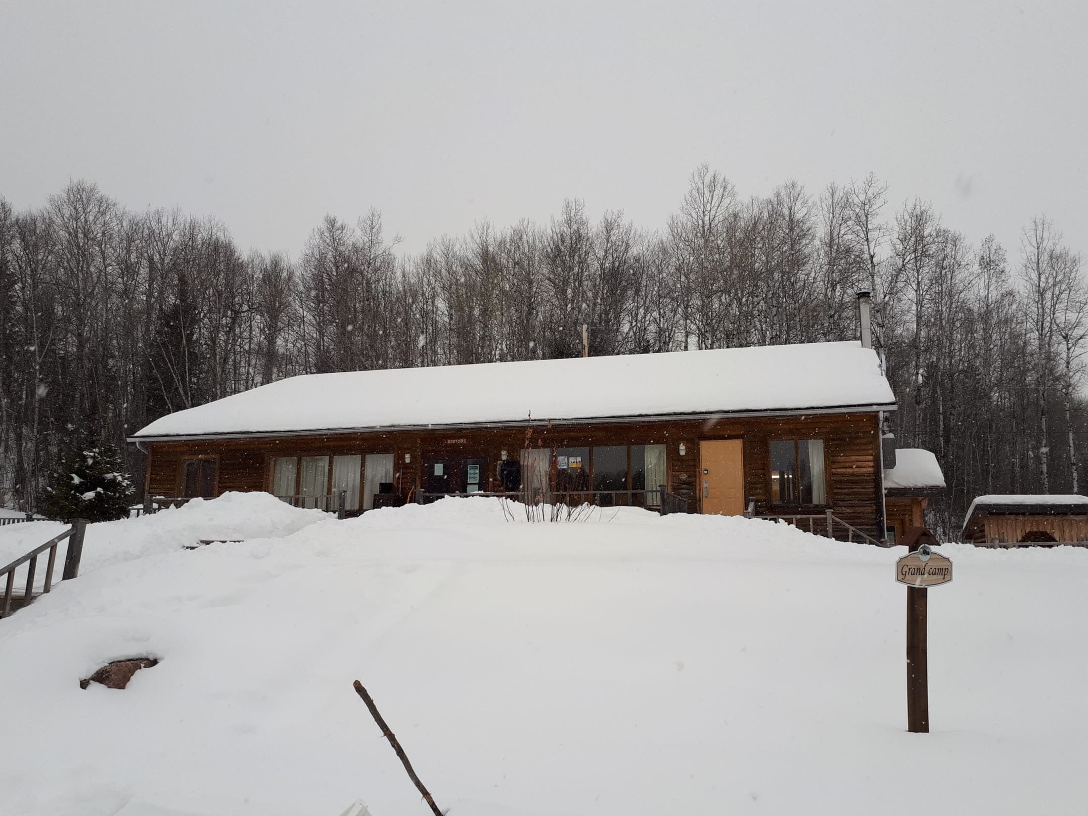 Le Grand Camp, long bâtiment de bois sous la neige, à l'orée du bois.