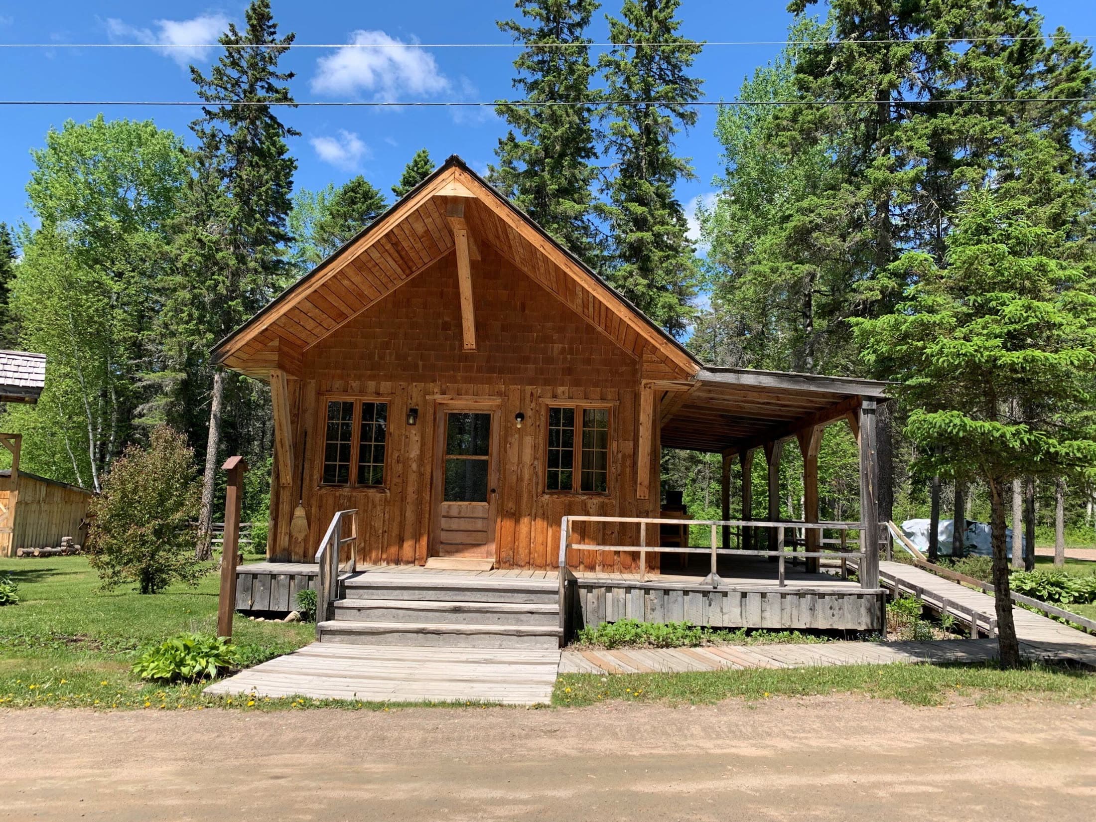 La Maison du Forgeron, petit chalet en bois avec galerie couverte, entouré de sapins.