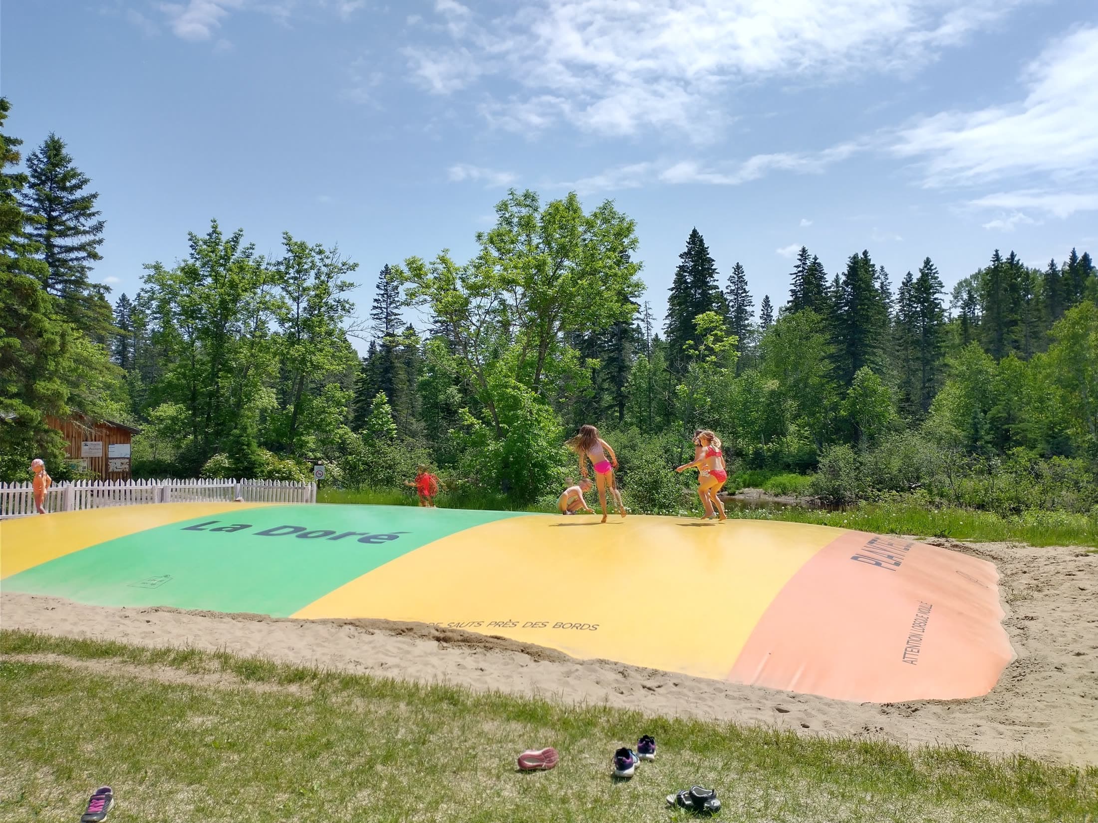 Des enfants sautent sur le tapis gonflable géant aux couleurs de La Doré, devant la forêt.