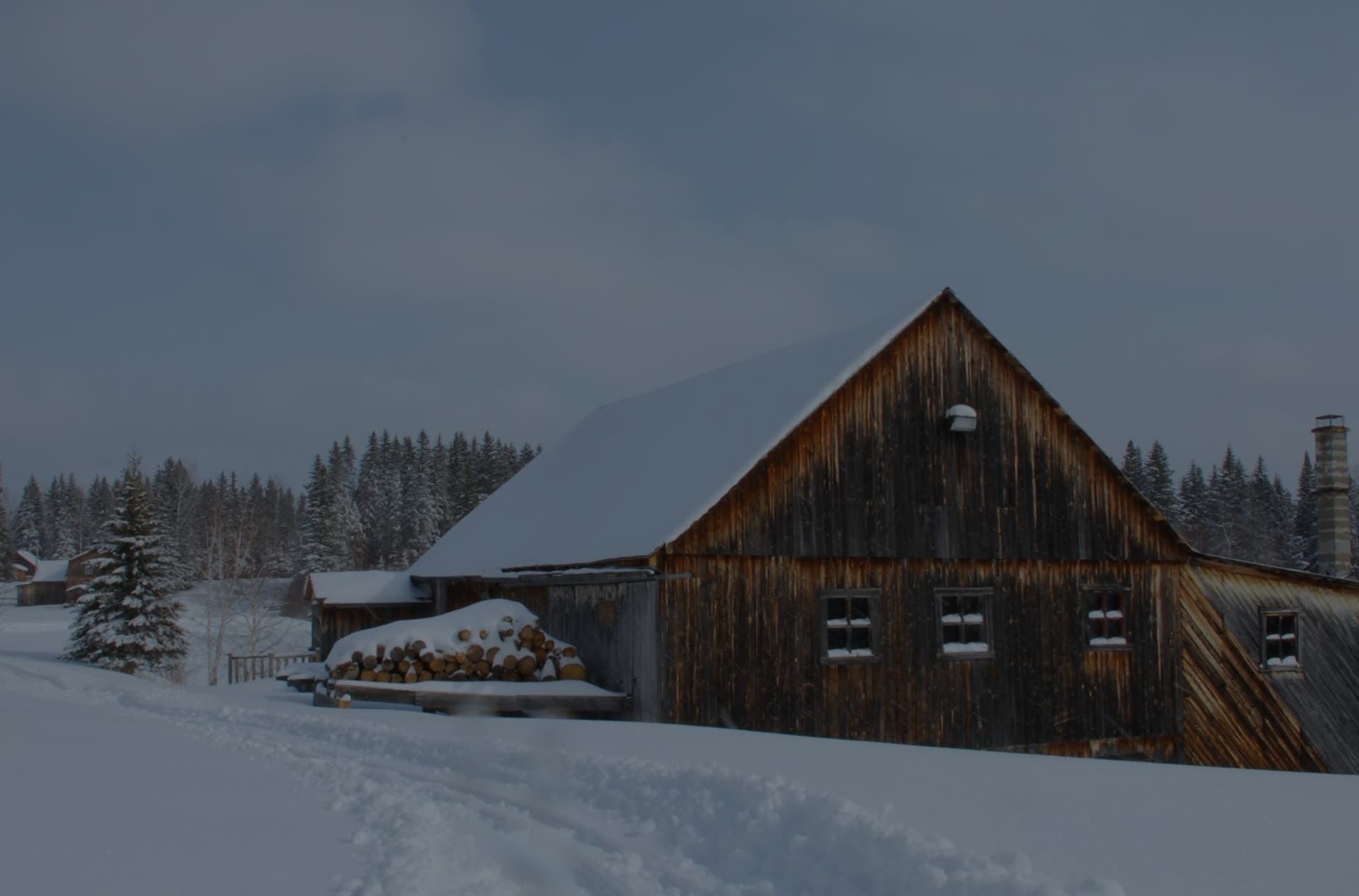 Le moulin de bois sous la neige, cordes de bois empilées le long du mur.