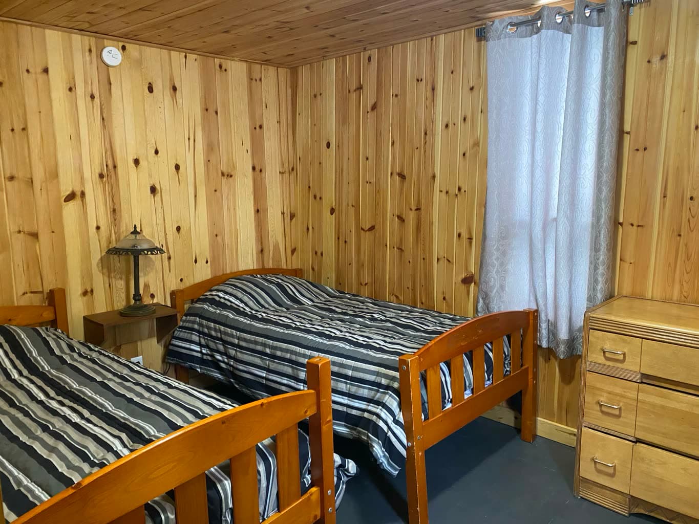Chambre avec deux lits simples, murs de pin et commode.