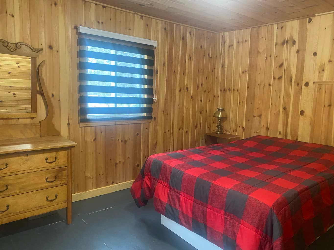 Chambre avec lit double, couvre-lit à carreaux rouges et commode à miroir.