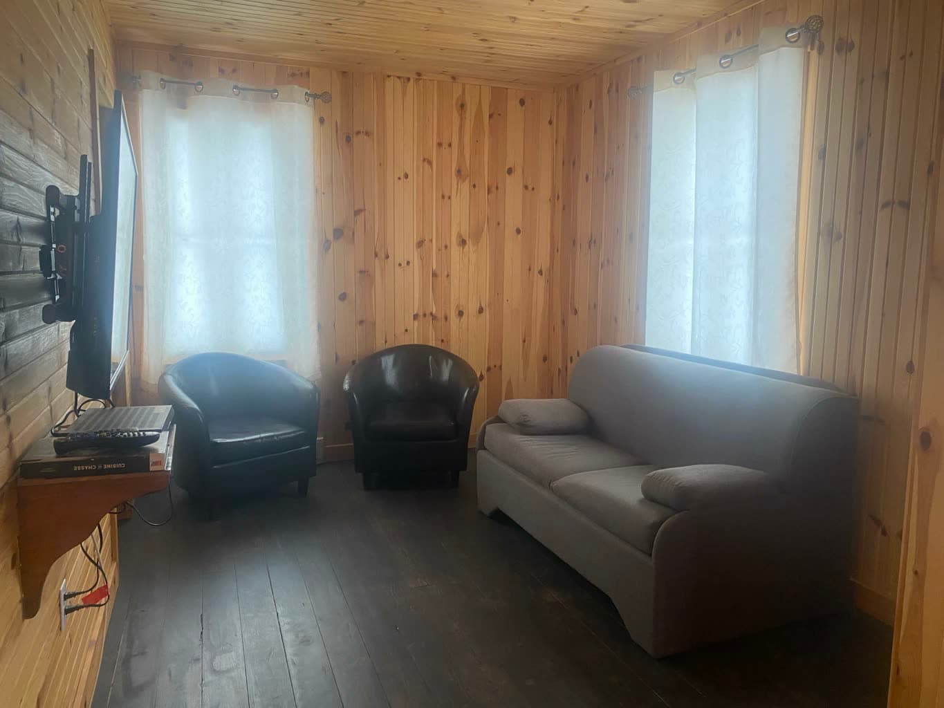 Le salon : deux fauteuils, un divan et la télévision, entre deux fenêtres.